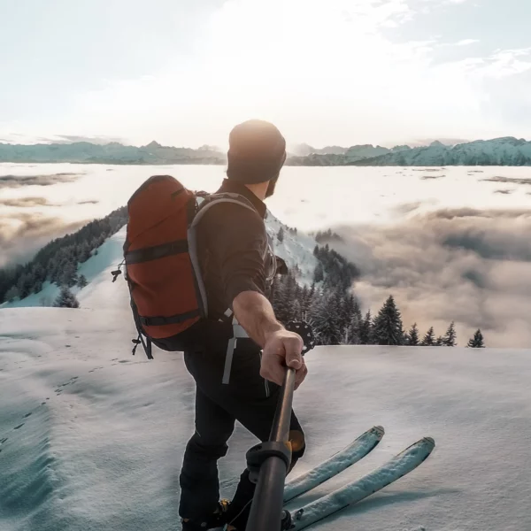 Skier at mountain summit with selfie stick, enjoying a vast snowy landscape. Perfect for showcasing winter sports and scenic views